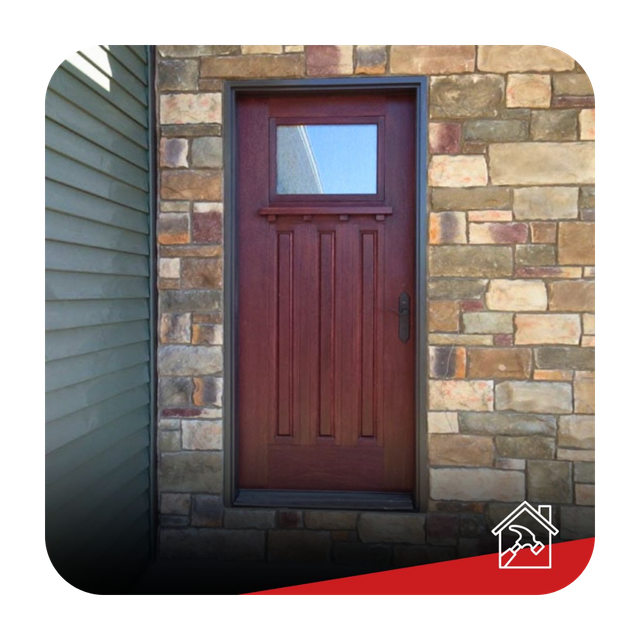 A red door with a small window is on a brick wall