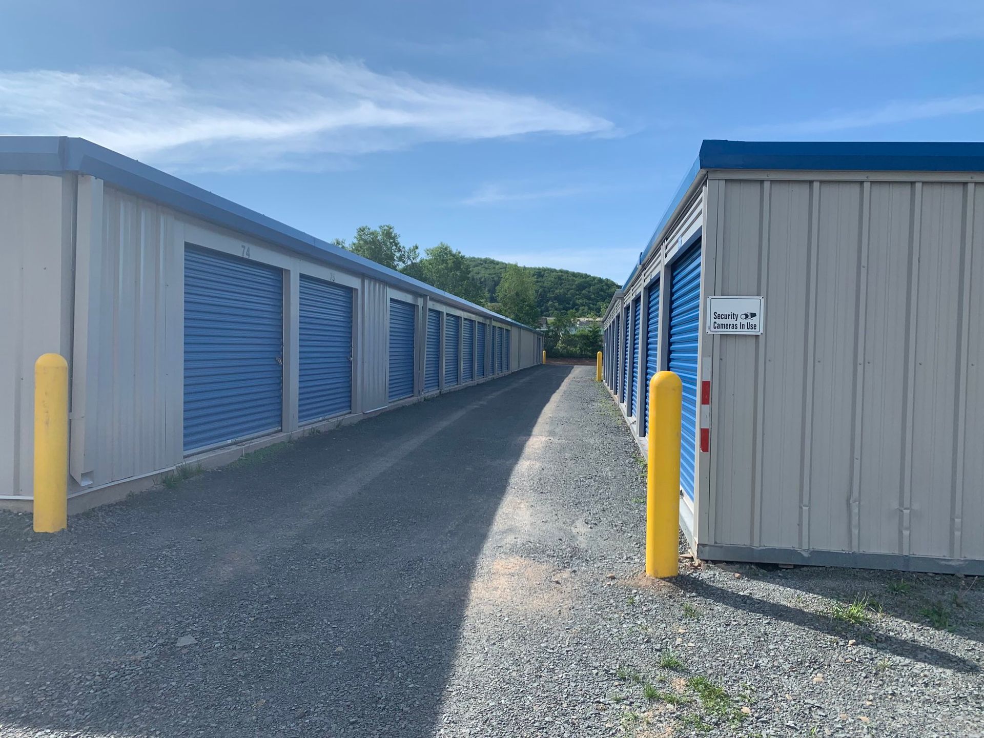 Two gray storage buildings with blue doors and yellow bollards at the corners of each building.