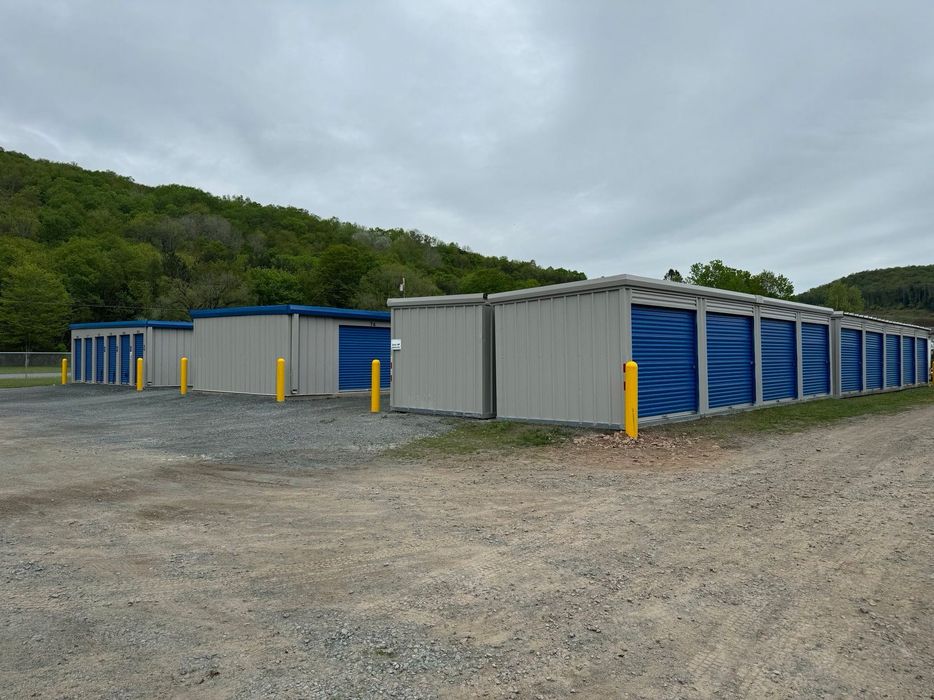 Three gray storage buildings with blue doors and yellow bollards at the corners of each building.