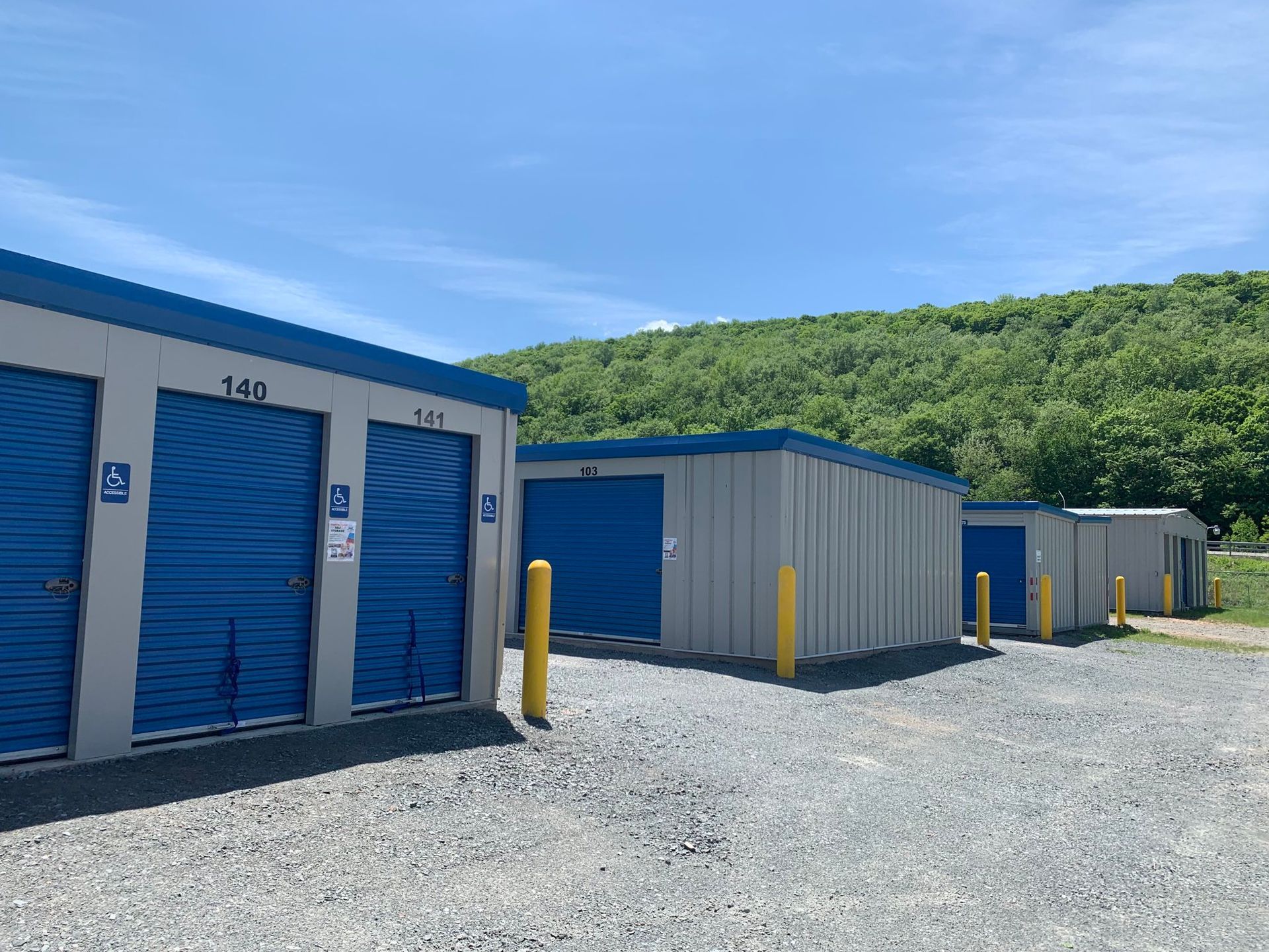 Four gray storage buildings with blue doors and yellow bollards at the corners of each building.