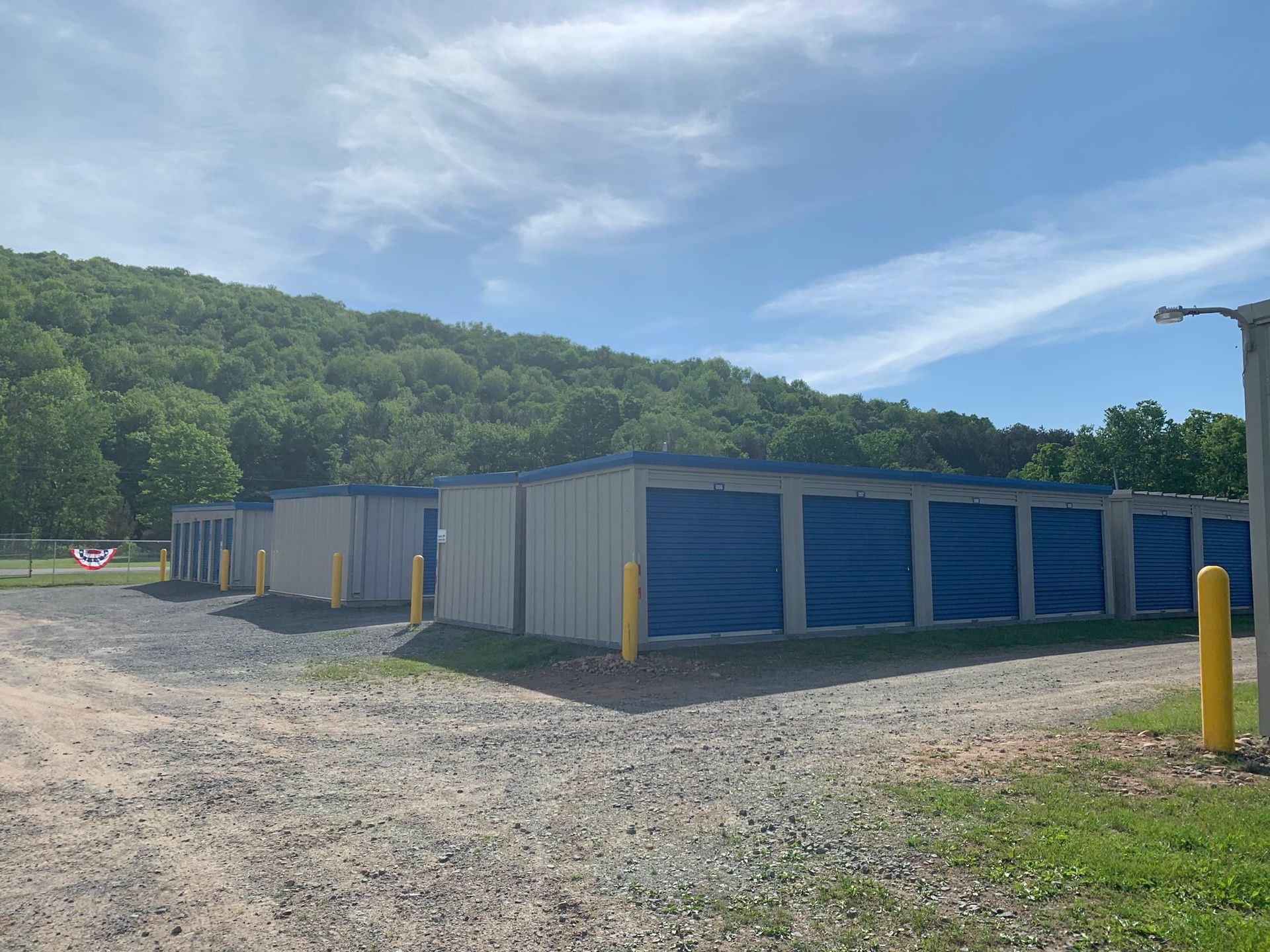 Three gray storage buildings with blue doors and yellow bollards at the corners of each building.