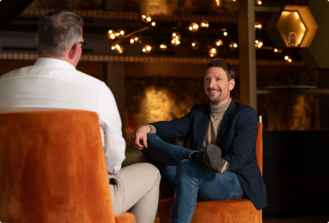 Two men are sitting in chairs talking to each other.