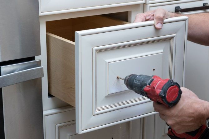 Person using a power drill to install a cabinet drawer front in a kitchen.
