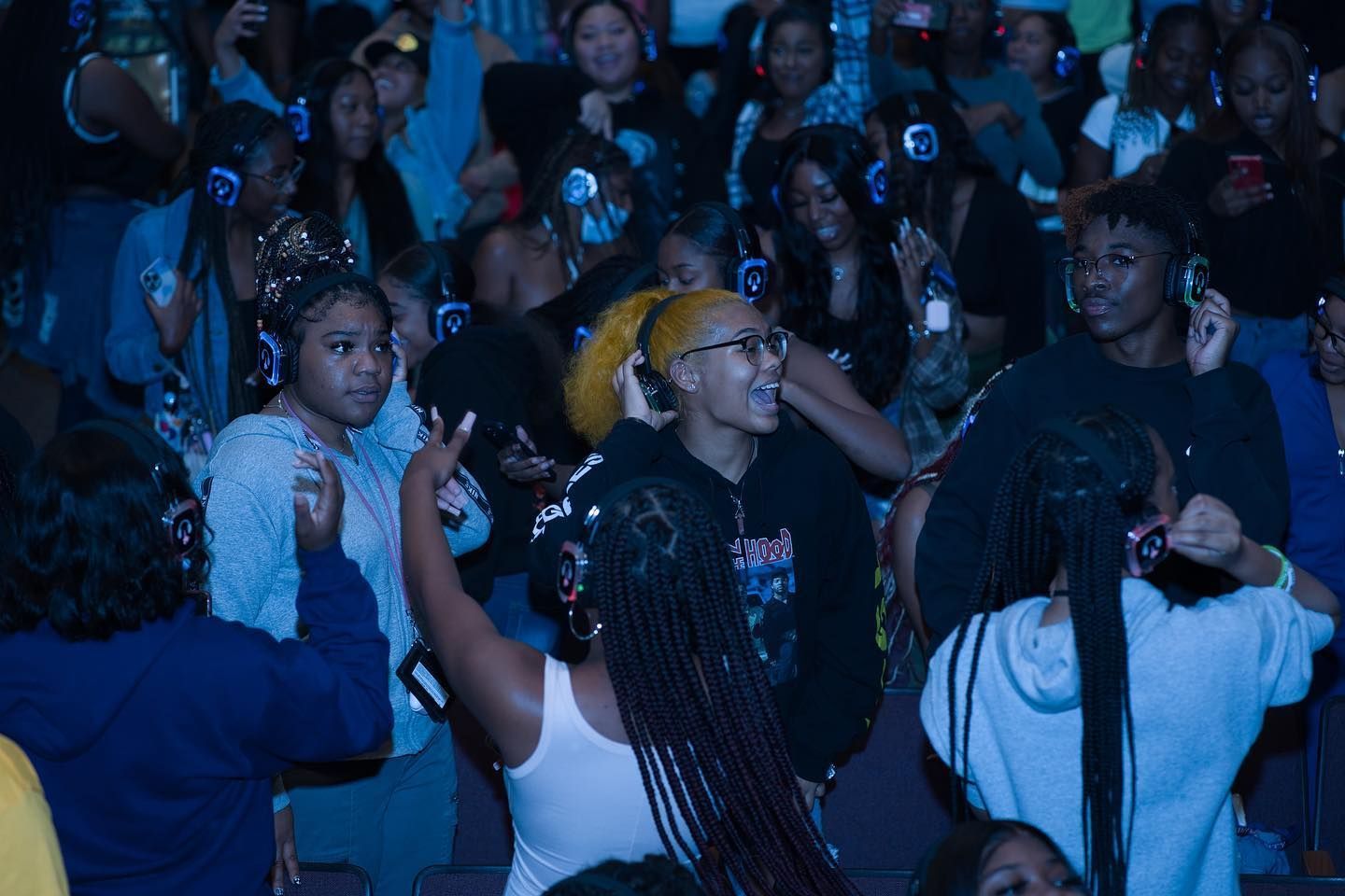 A crowd of people wearing headphones are dancing in a dark room.