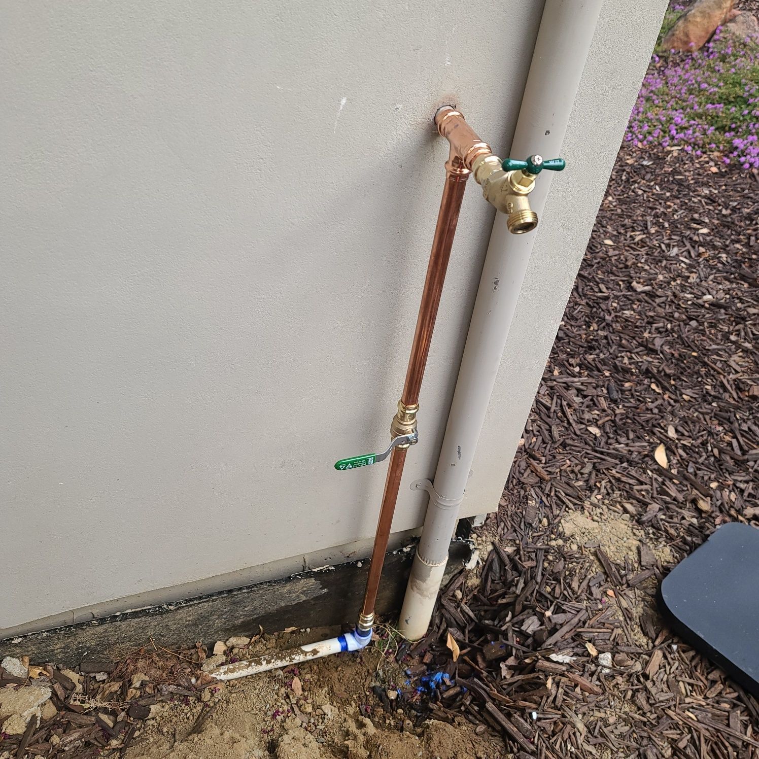 Copper water pipes with valves against a tan stucco wall. One valve is green, the other gold.