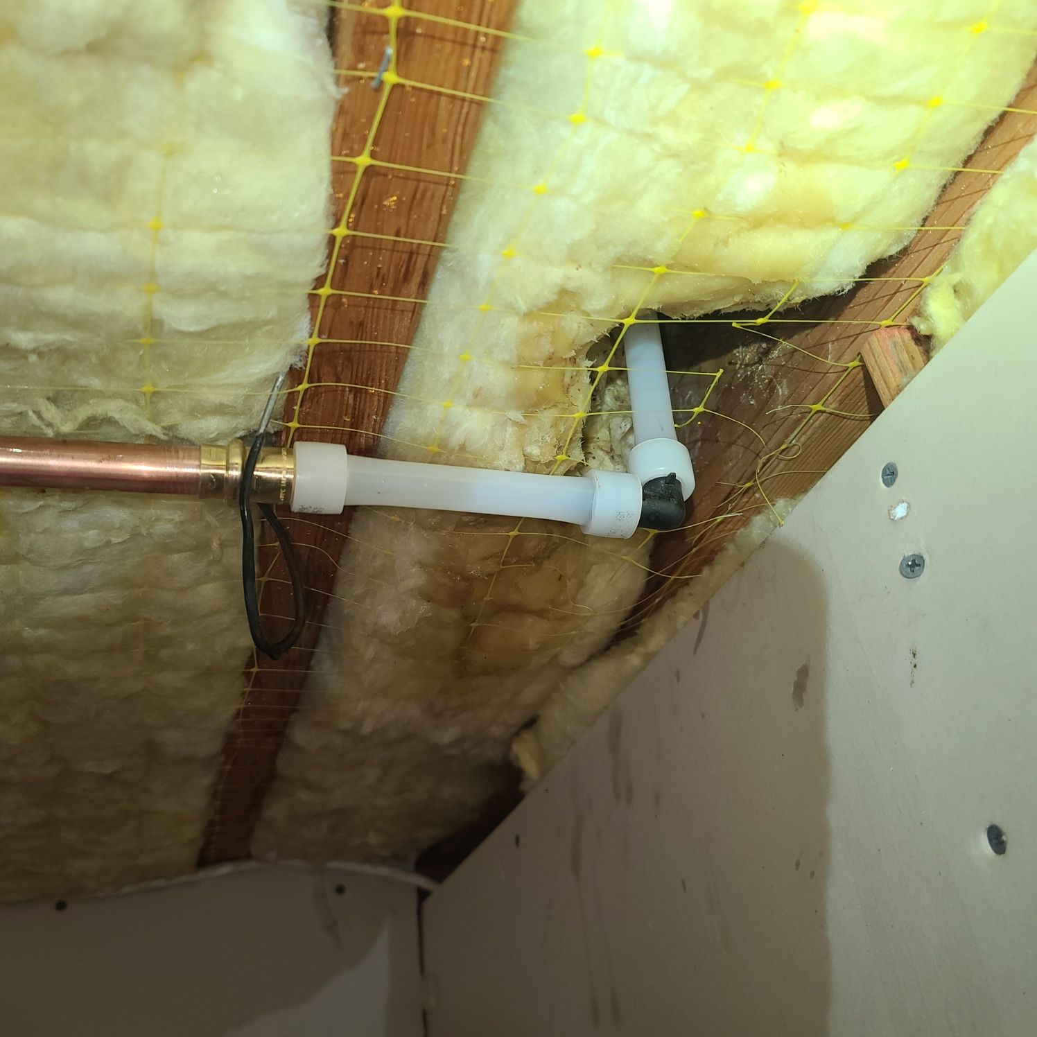 Plumbing pipes in attic. Copper and white pipes attached to wooden beams and insulation.