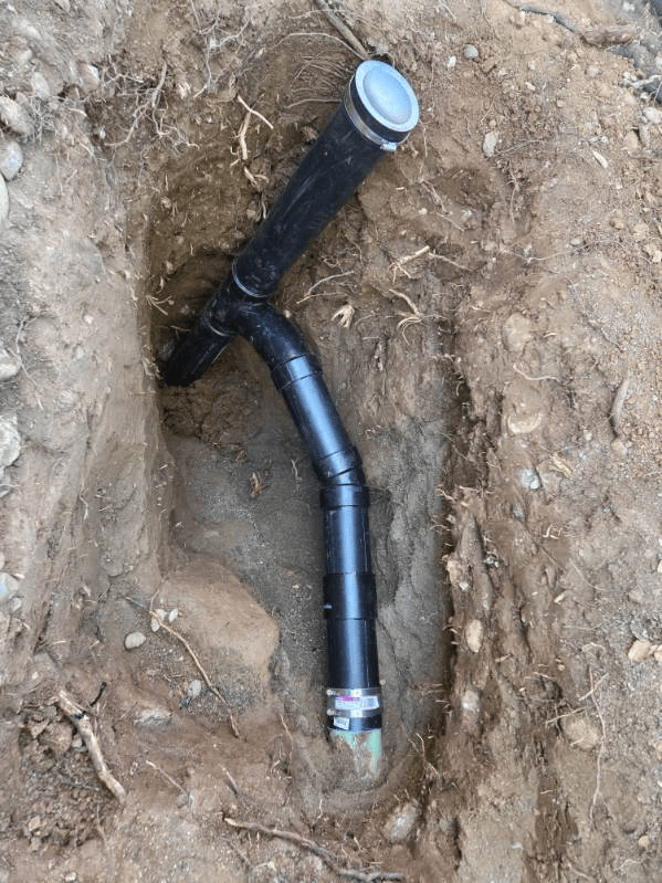 Black plumbing pipes installed in a dirt trench, likely for drainage.