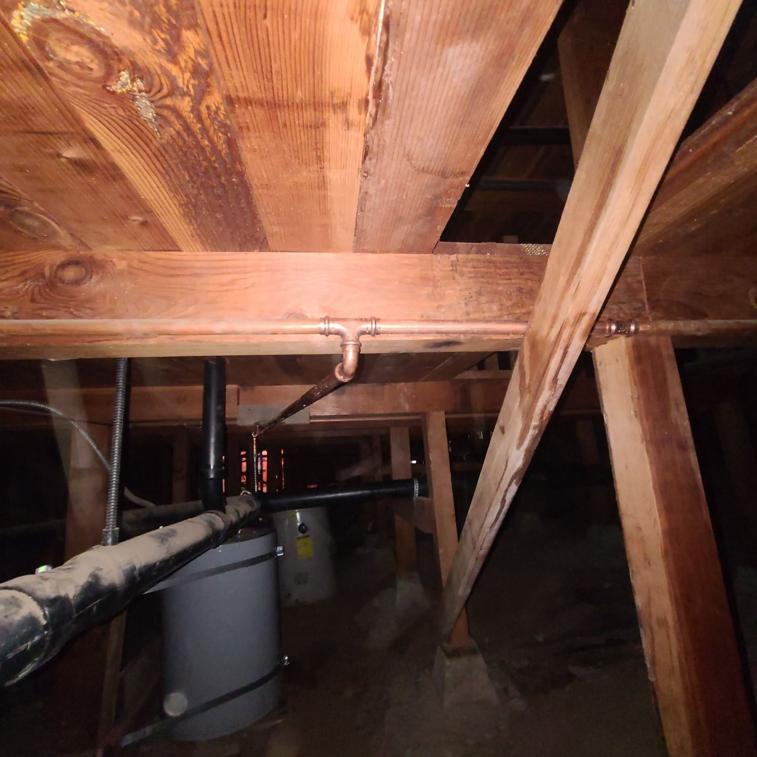 Wooden house beams and plumbing in a crawl space. Water heater is visible.