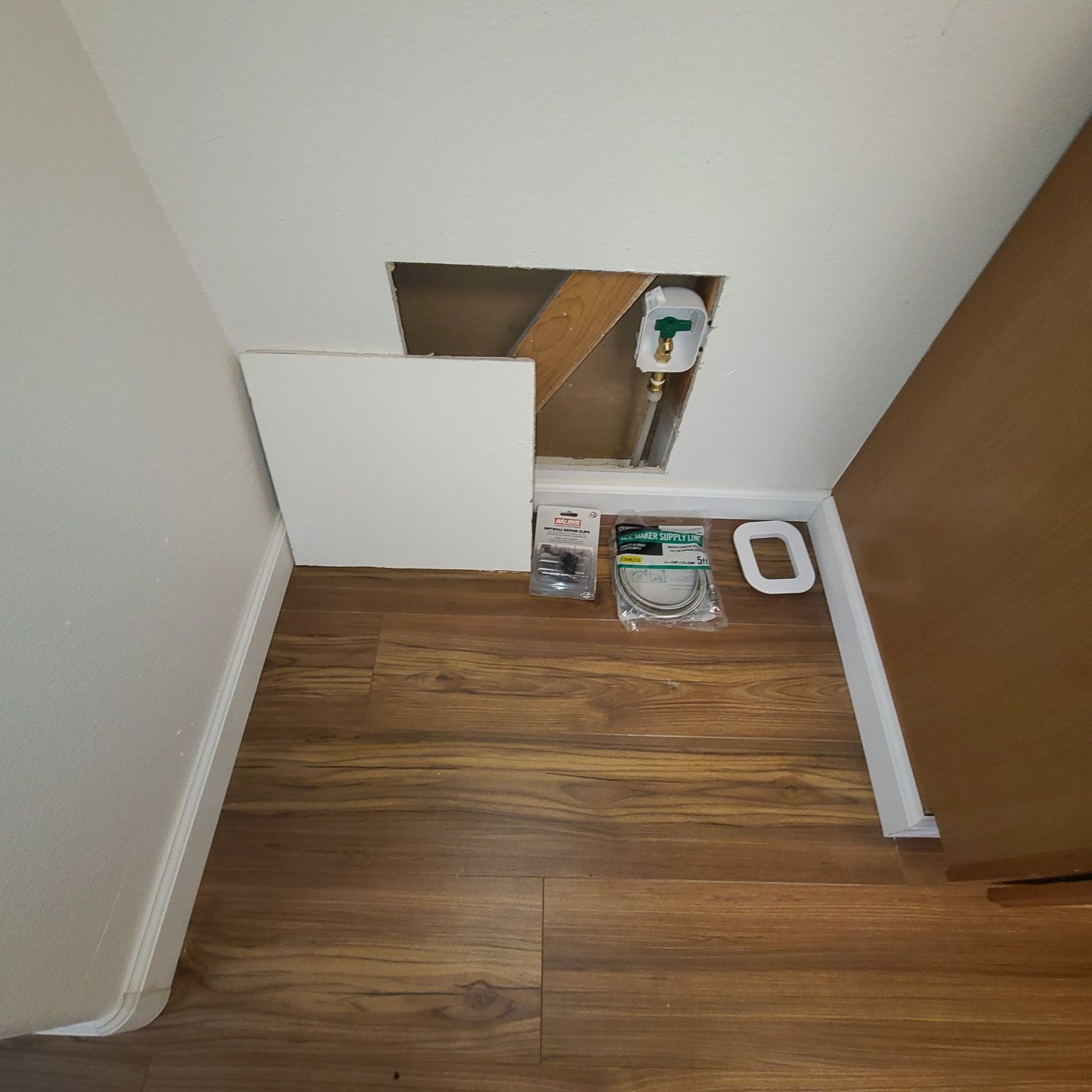 Laundry area with access panel, plumbing, flooring, and supplies on the floor.