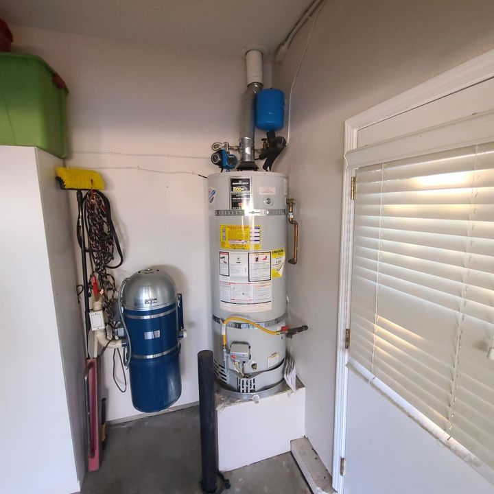 A water heater inside a utility room, with a blue expansion tank on top.