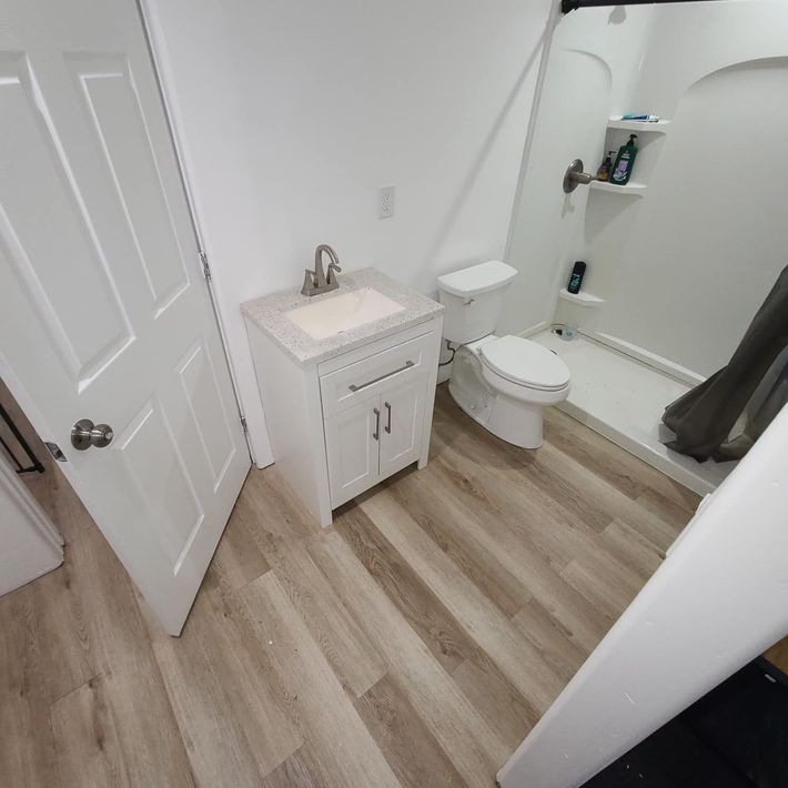 Toilet in a bathroom with light-colored flooring and a shower enclosure to the right.