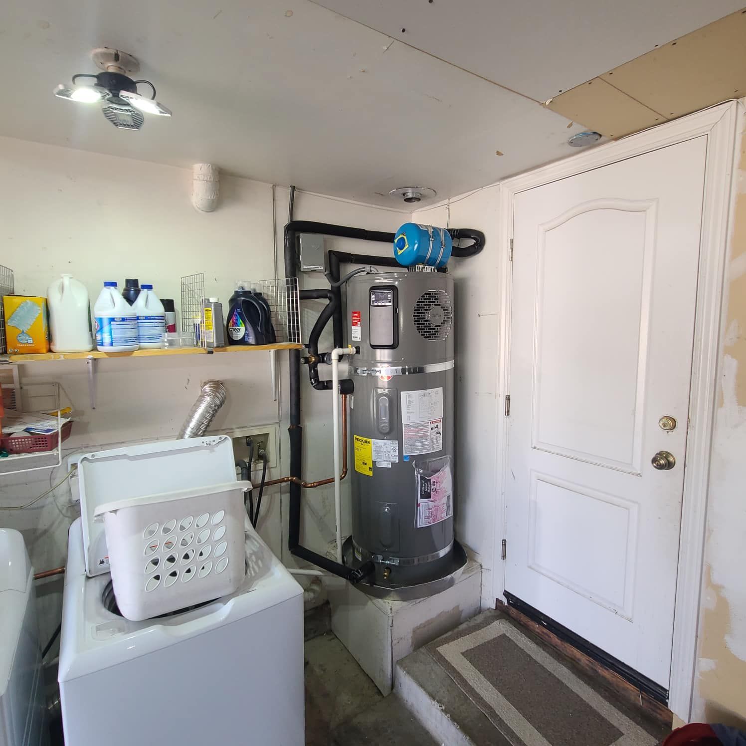 A wall-mounted, white tankless water heater installed in a basement. 