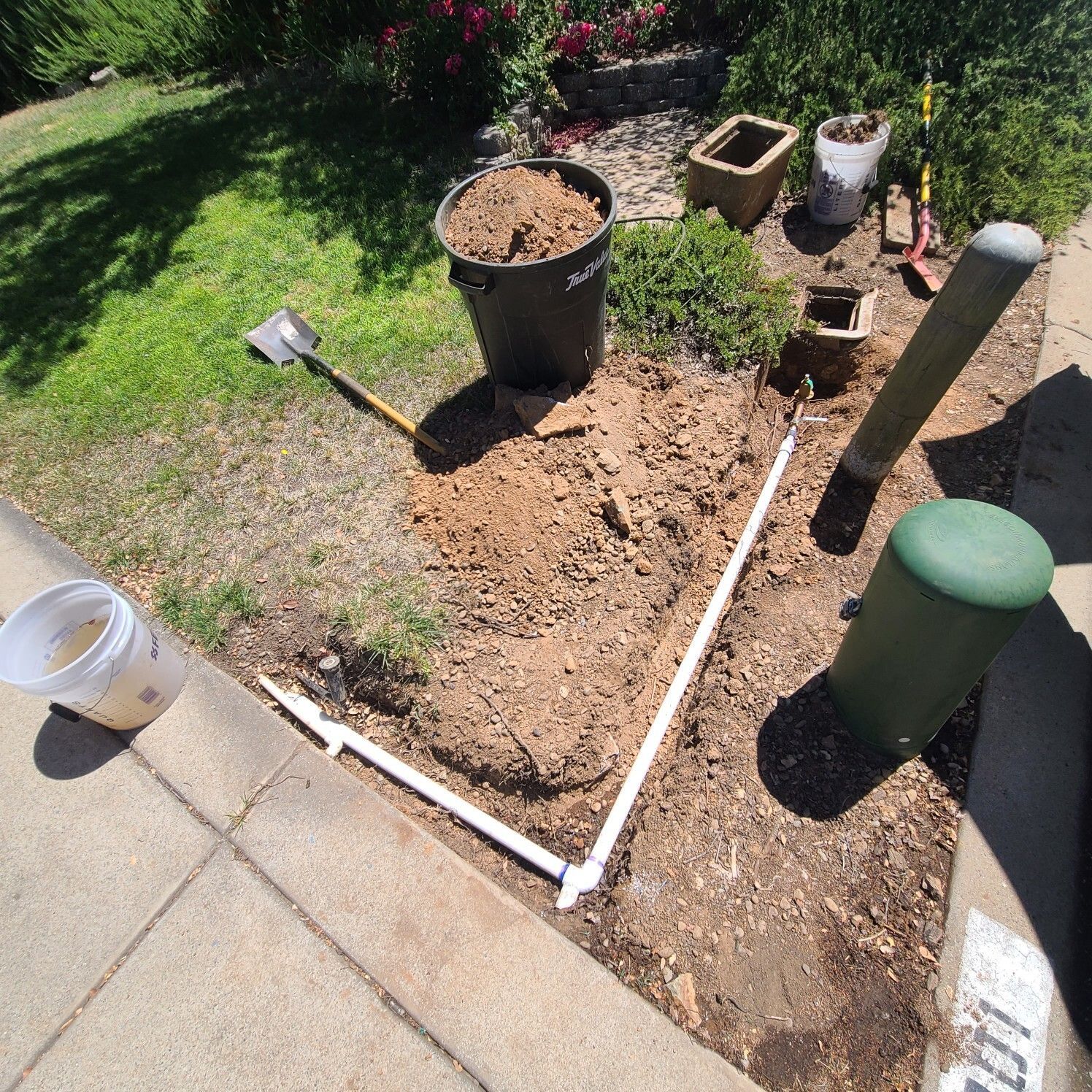 A garden bed being worked on, with a shovel, bucket of soil, and PVC pipe laid out.