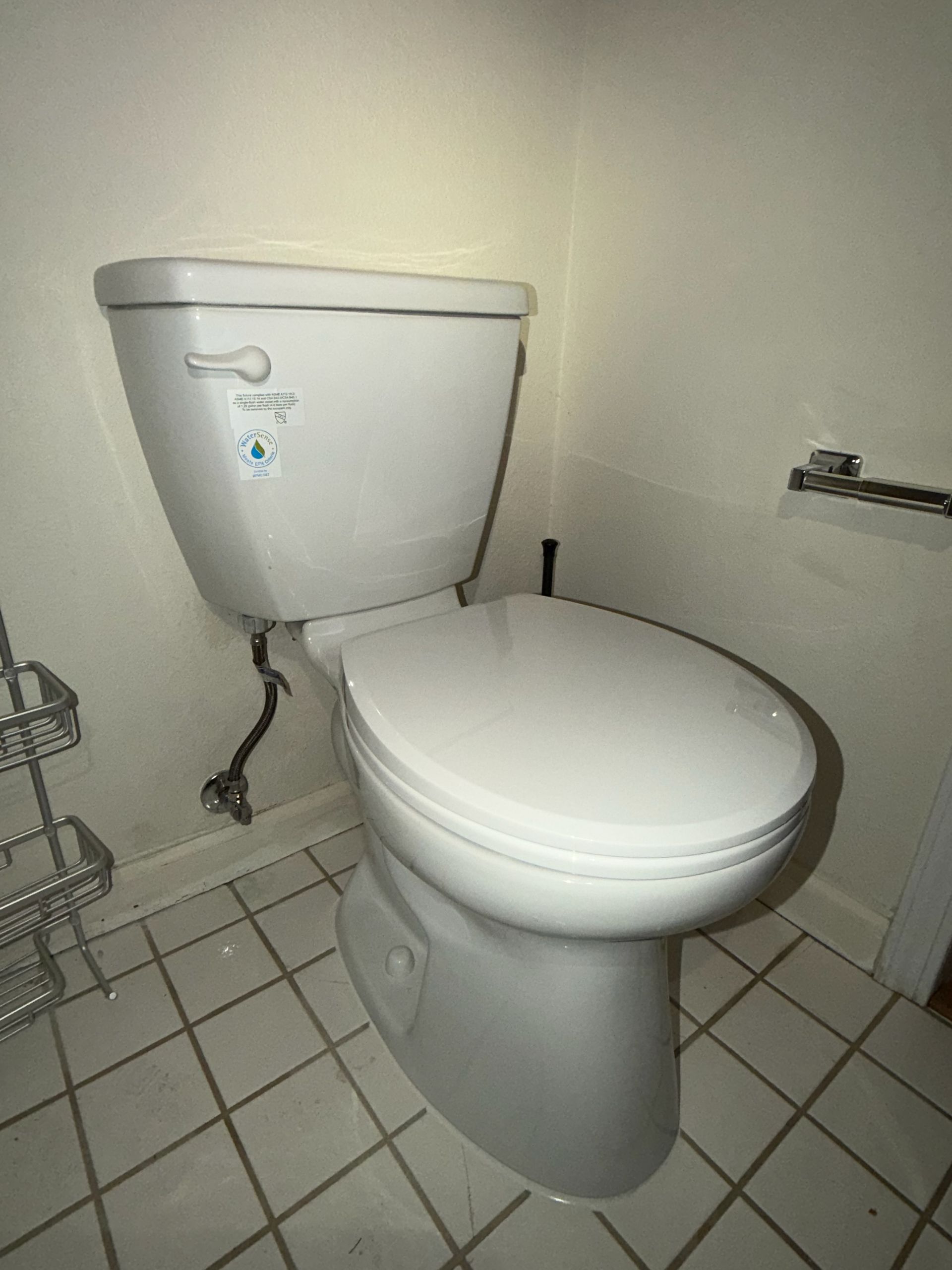 A white porcelain toilet in a tiled bathroom with a wall-mounted toilet paper holder.