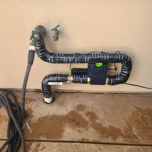 Hand turning a chrome shut-off valve attached to a wall. A flexible metal hose extends from the valve.