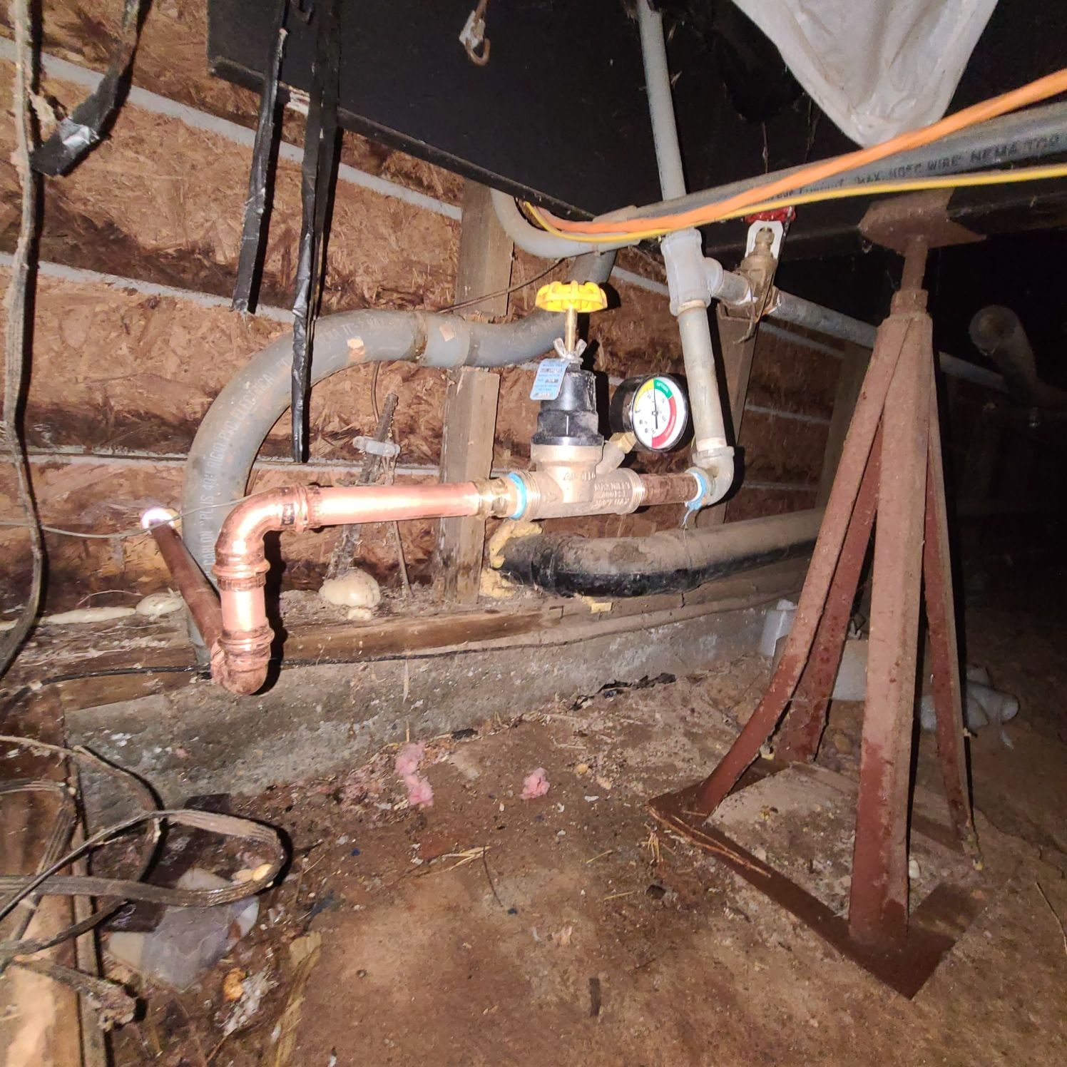 Copper pipes and valves in a utility area with an attached pressure gauge.