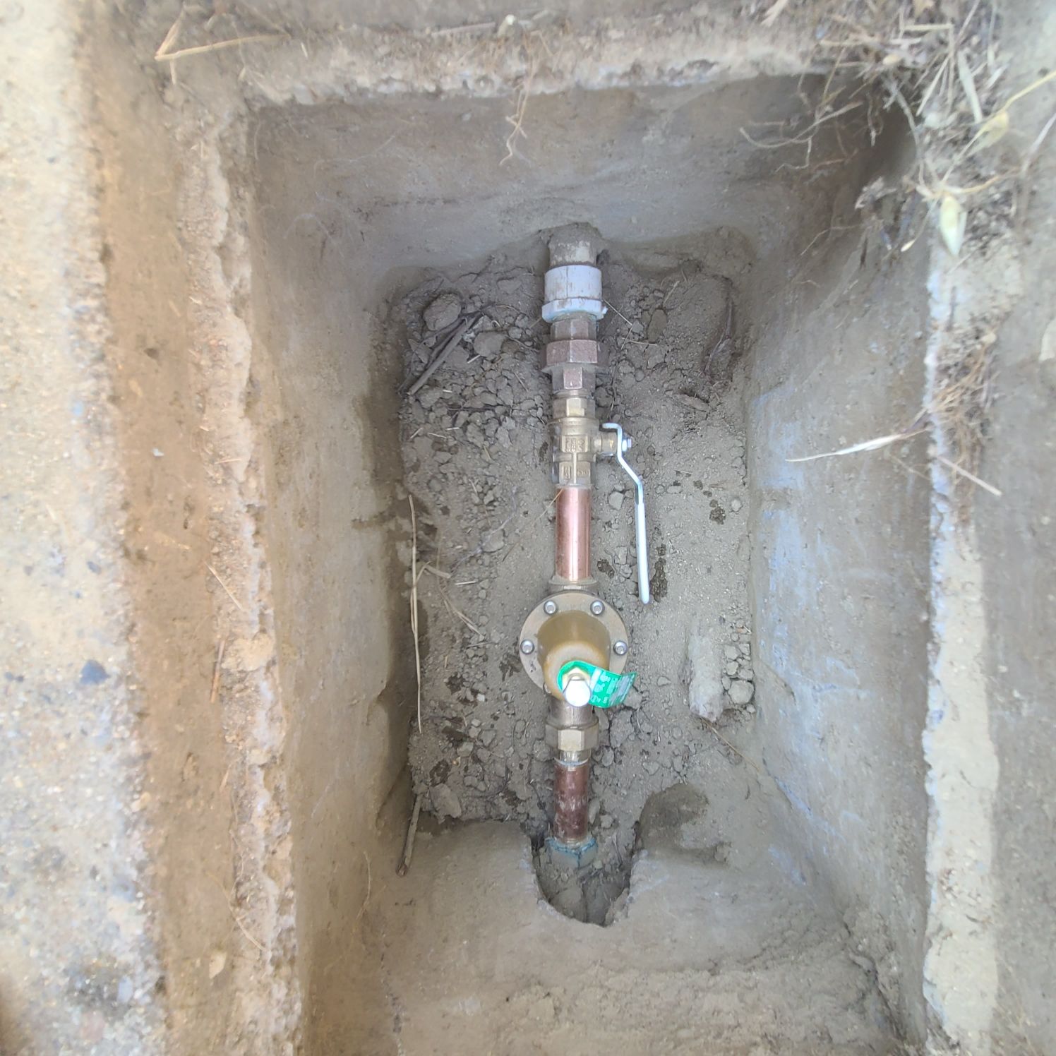 A water meter and pipes are installed in a rectangular hole in the ground