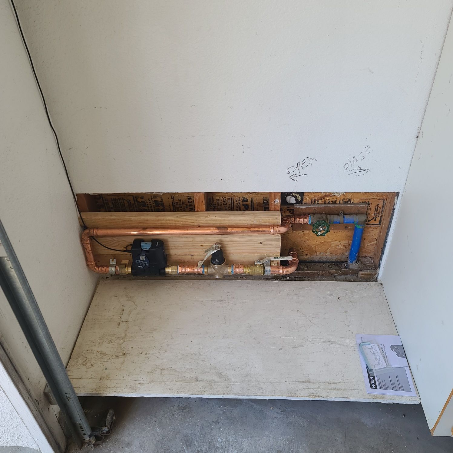 Plumbing system installed in a recessed wall. Copper pipes and black valve are visible; the wall is white and the flooring is cement.