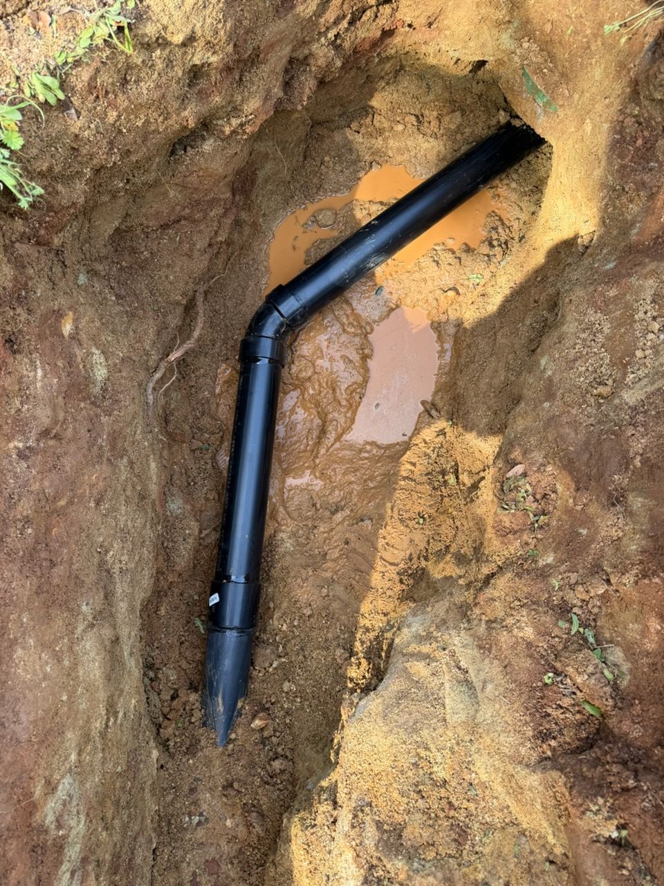 Black pipe installed in a dirt trench, angled towards a hole.