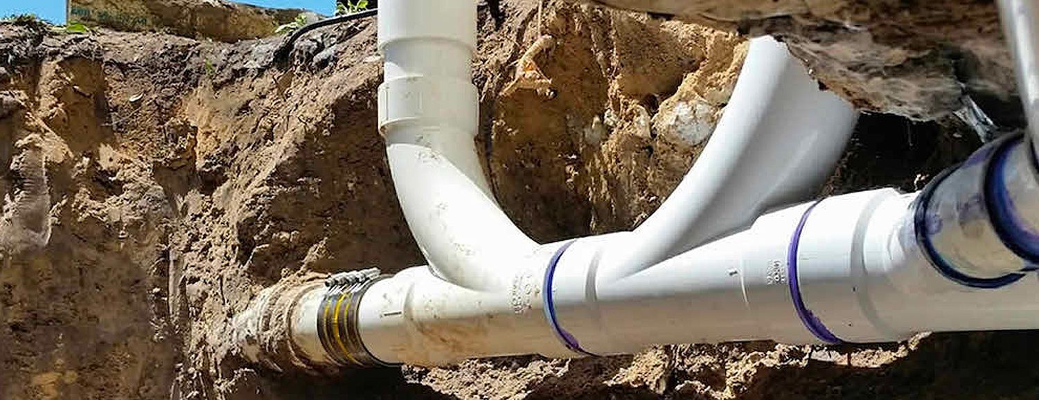 Broken PVC pipes in a dirt trench, with water leaking from the cracks.