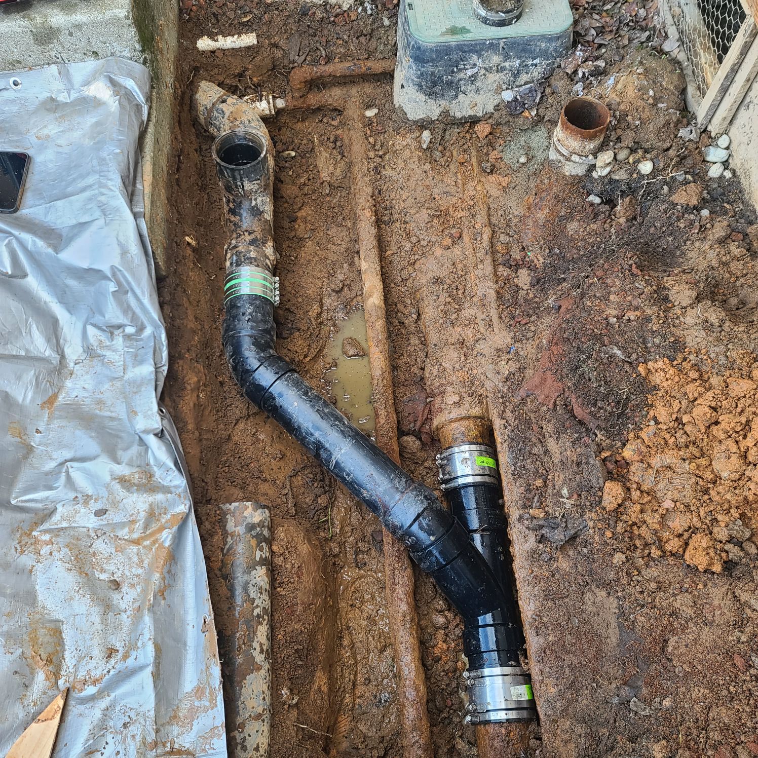 Black plumbing pipes installed in a trench, dirt and gravel surrounding.