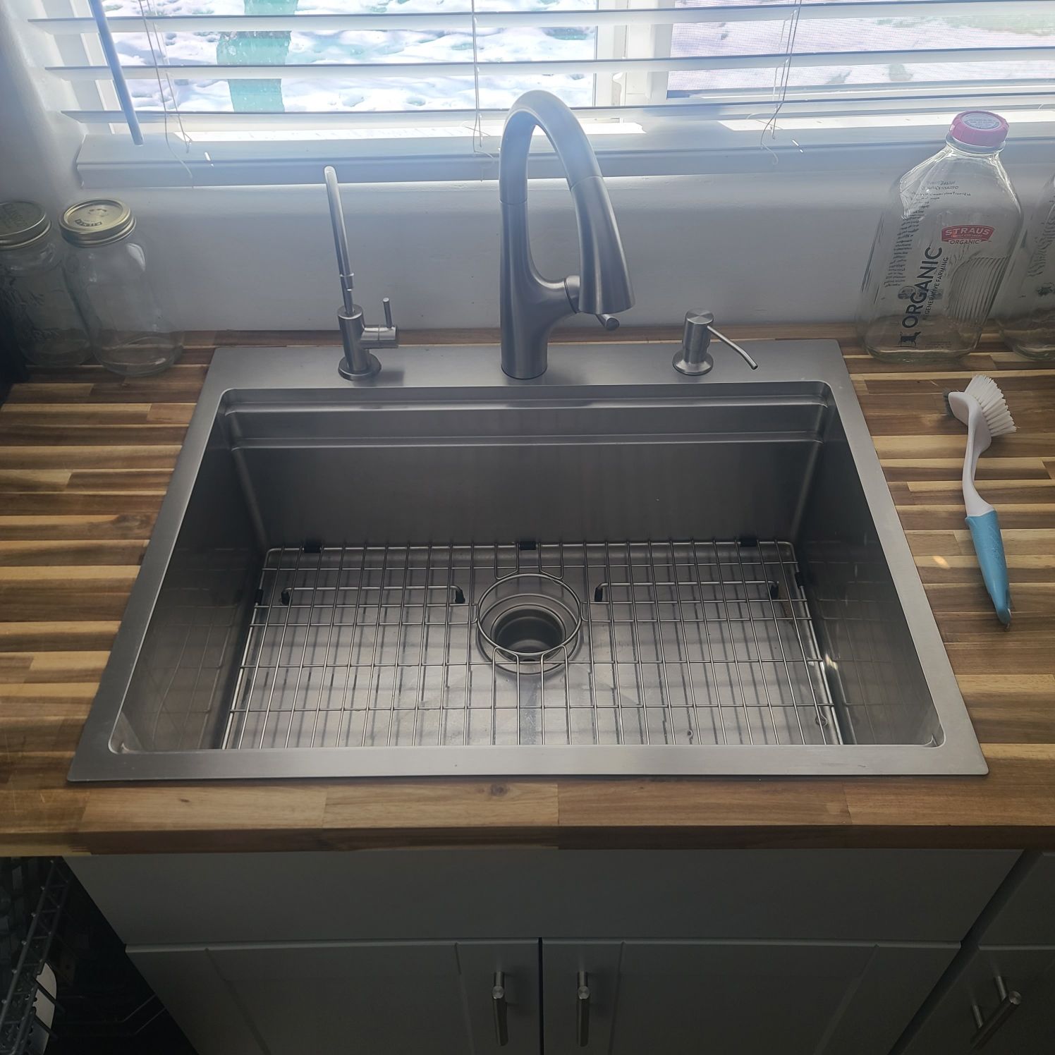 Stainless steel kitchen sink with a grid, faucet, and soap dispenser on a wooden countertop.