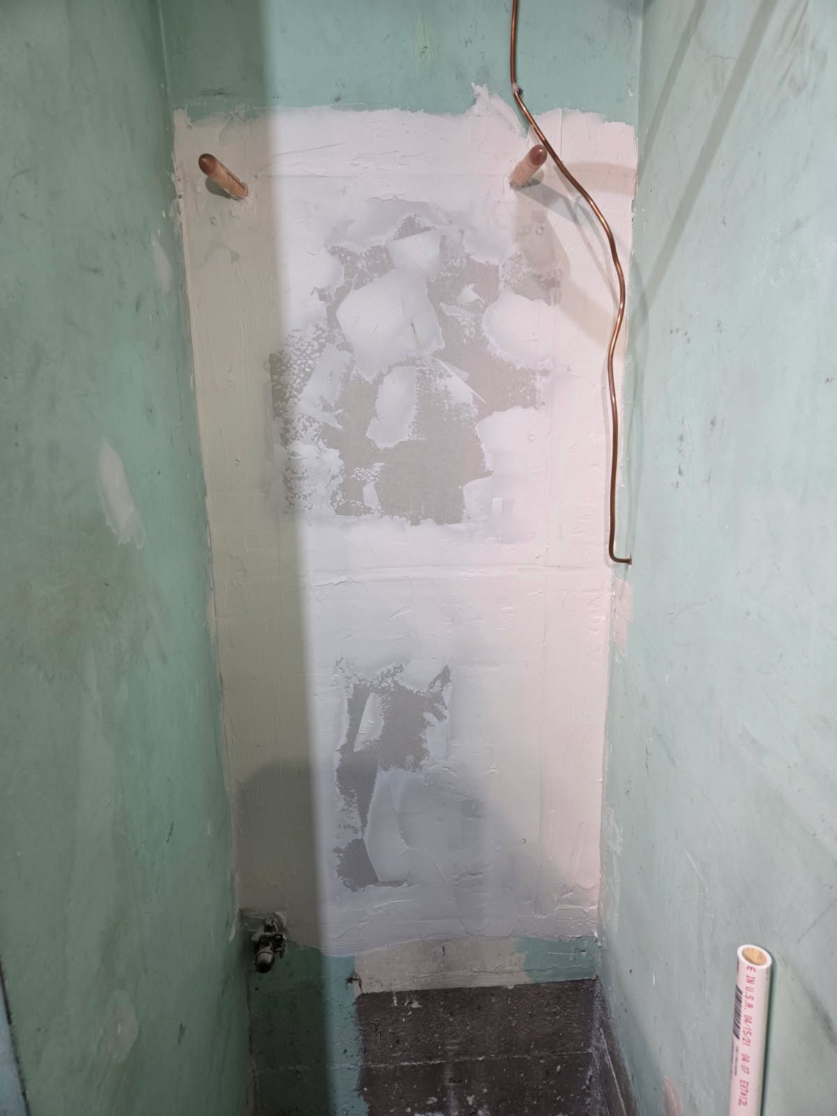 Narrow room with walls painted in light green and white. Partially plastered central wall.