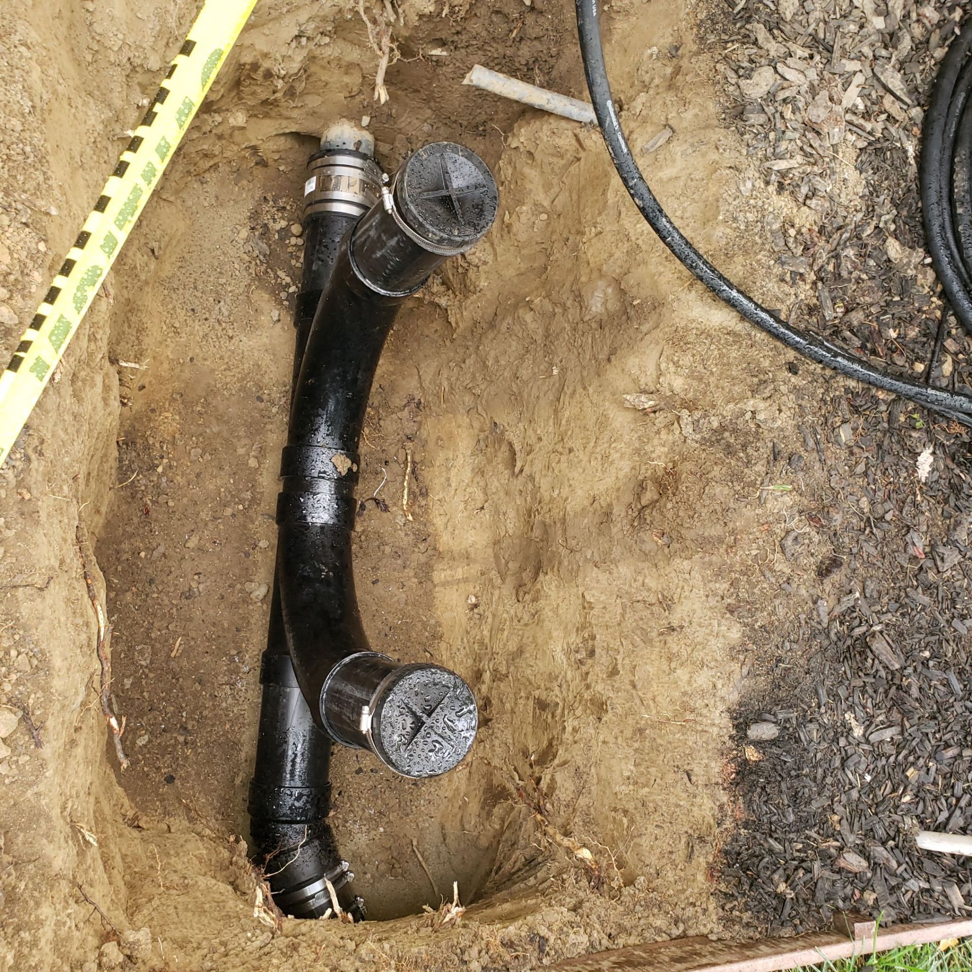 Black pipes in a dirt hole, likely a plumbing project.