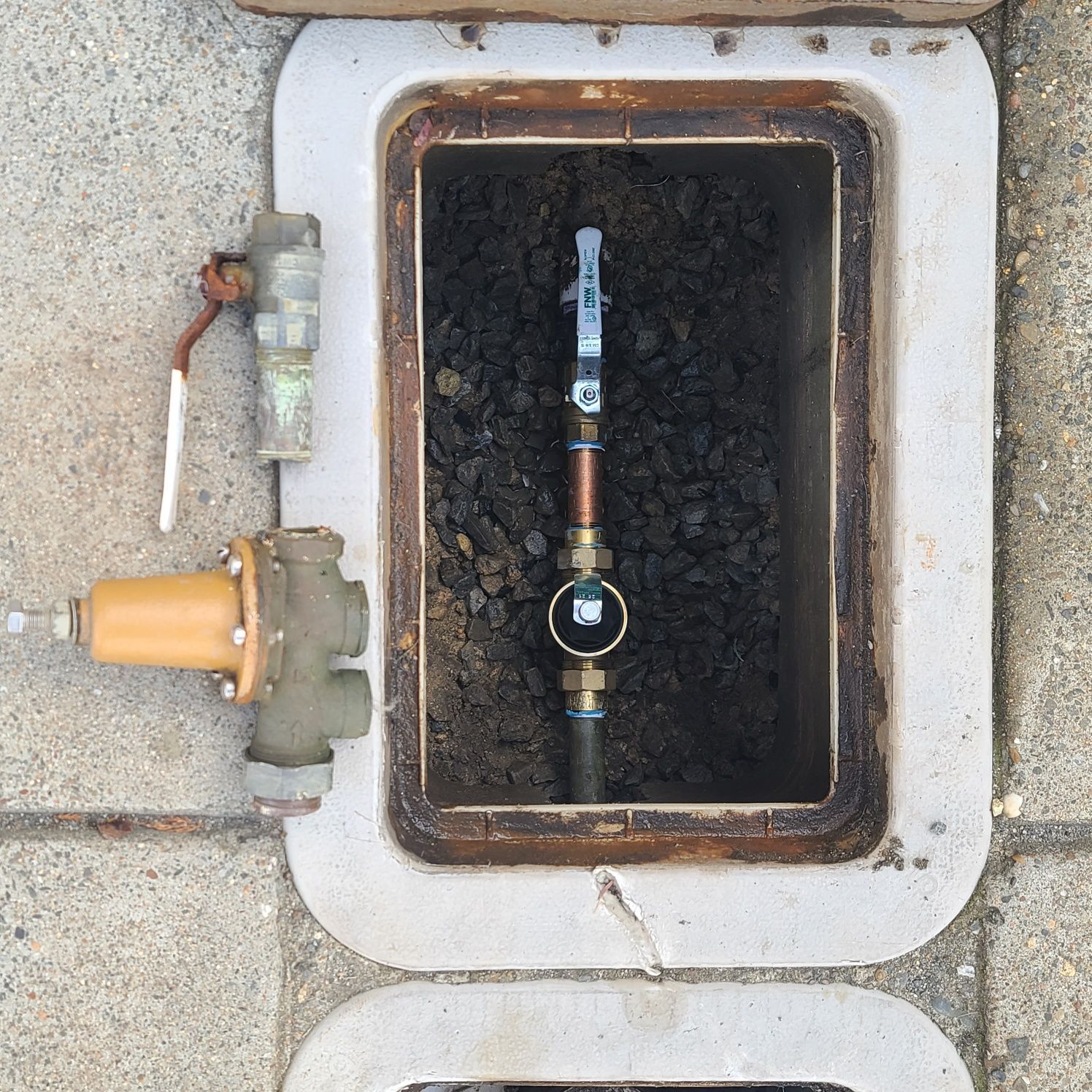 Water meter and pipes inside a rectangular, concrete utility box.