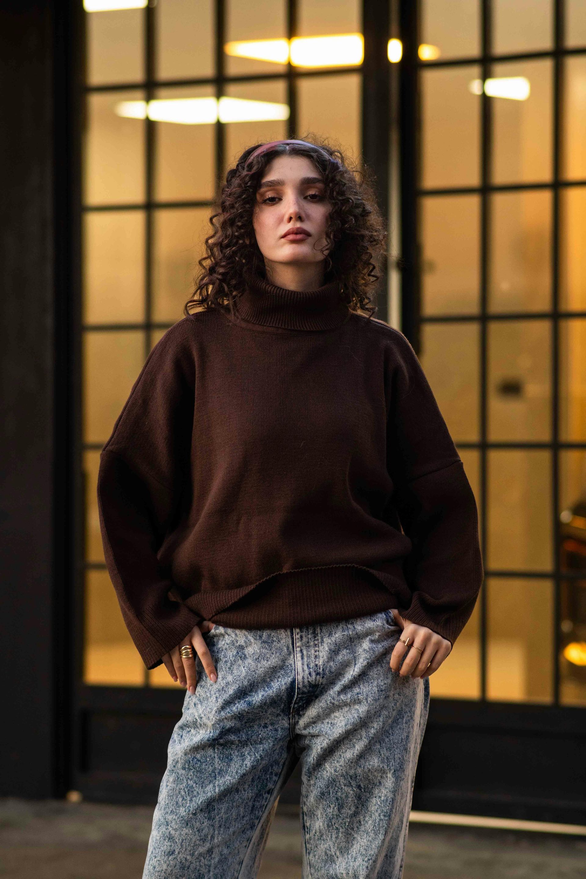 Plumber in red cap and shirt working under a white sink, connecting pipes. Gray overalls, focused expression.