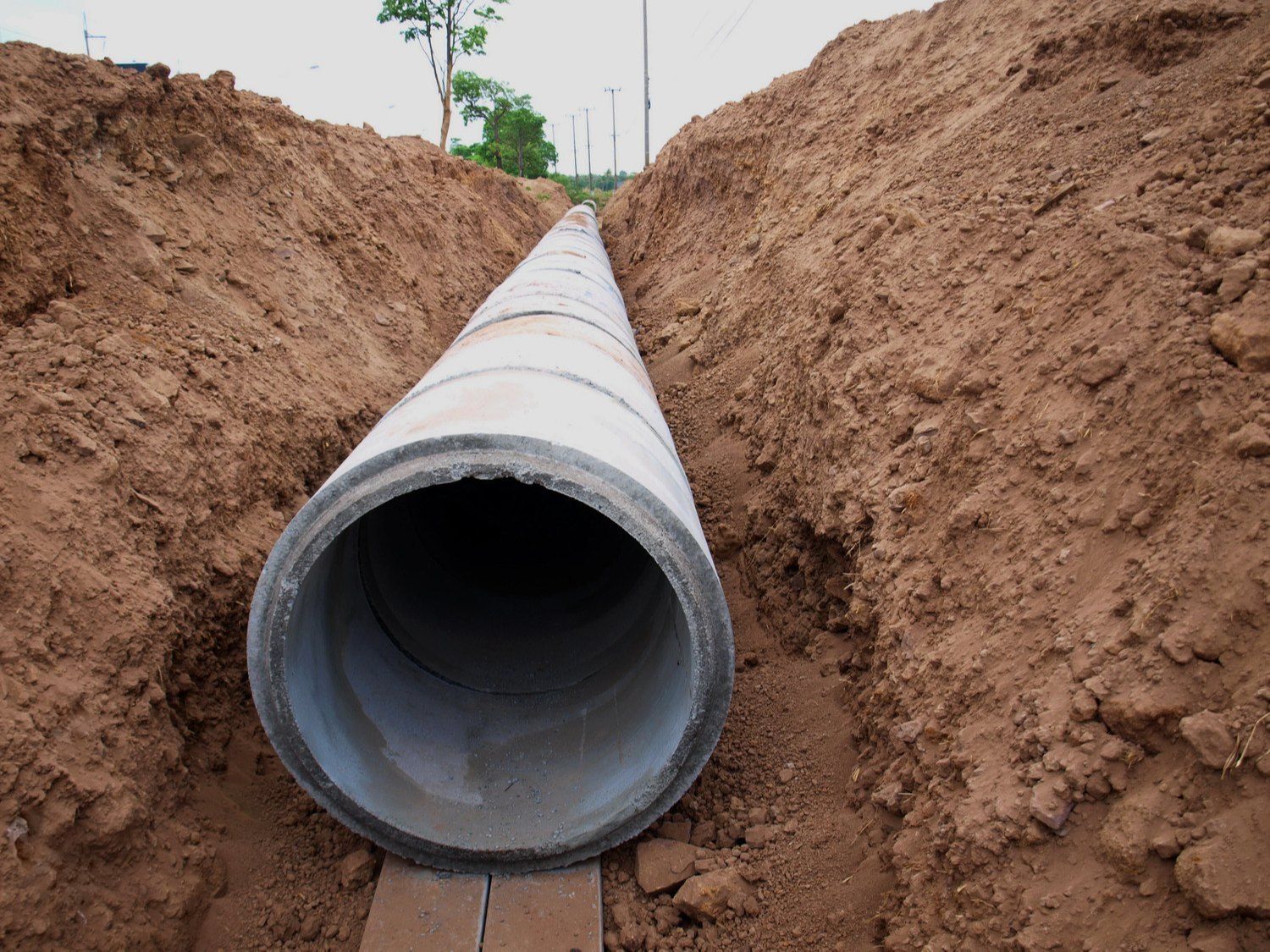 Large concrete pipe installed in an open trench, brown earth on either side.