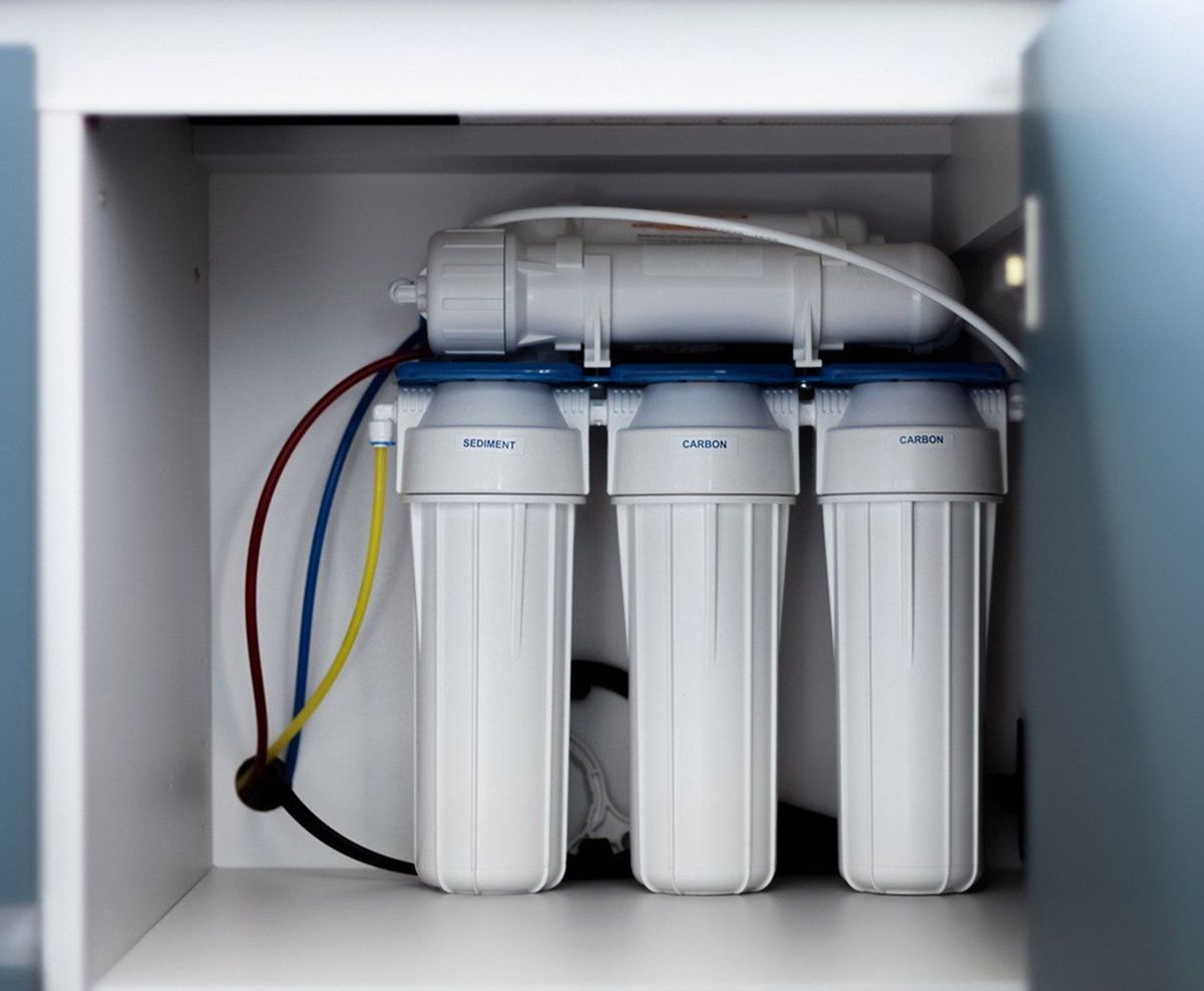 Water filtration system installed in a cabinet; three white filter housings with connecting tubes.