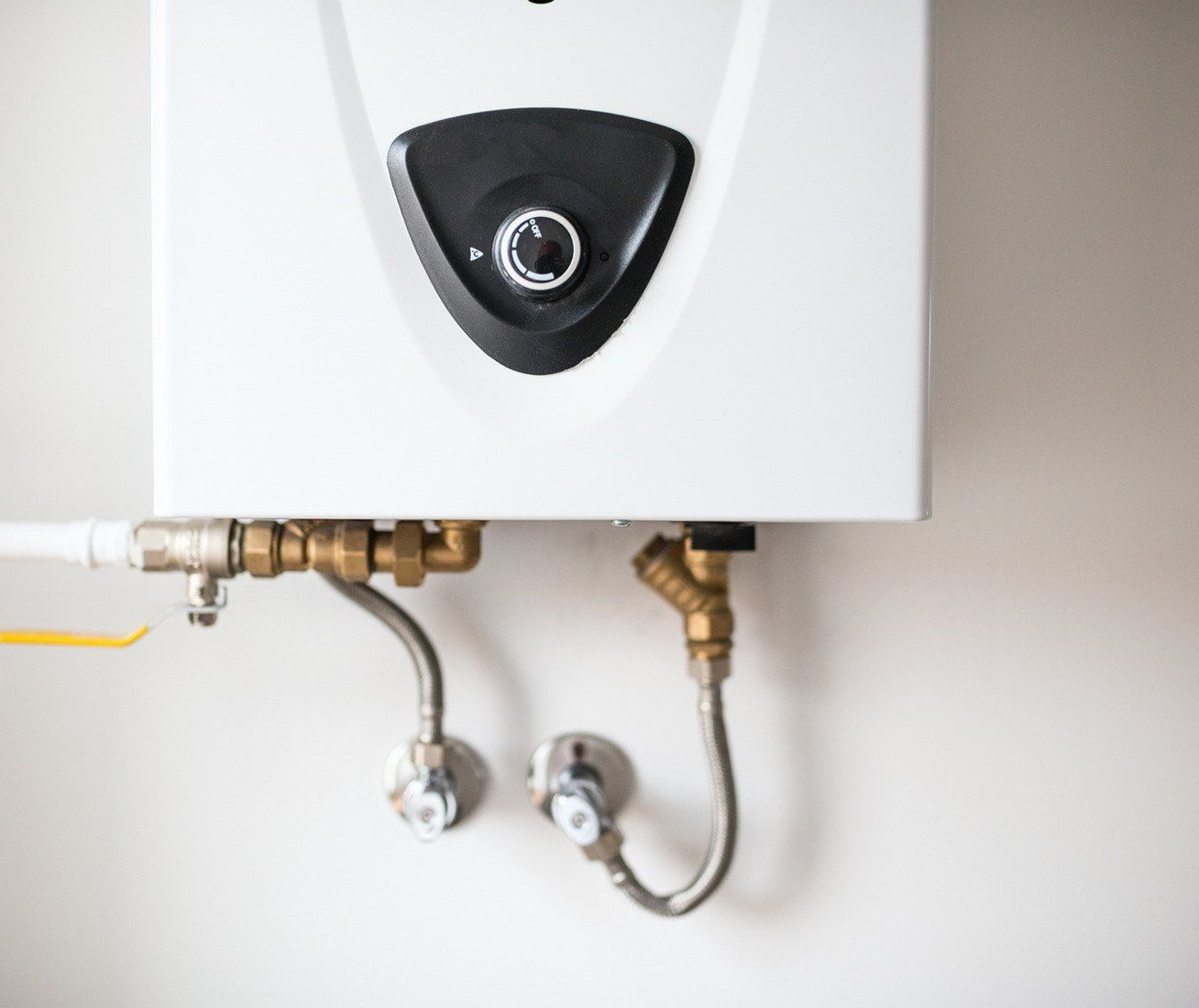 White water heater mounted on a white wall with connected pipes and valves.