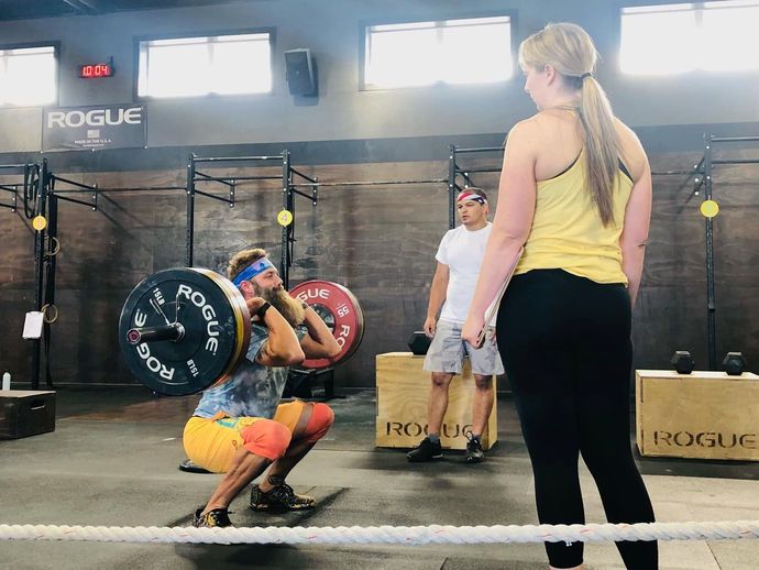 A woman squatting with a barbell in a gym while a man watches.