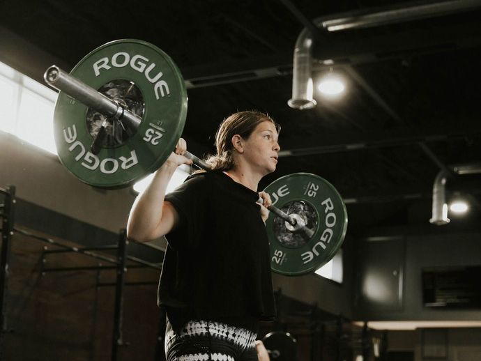 A woman is lifting a barbell over her head in a gym.