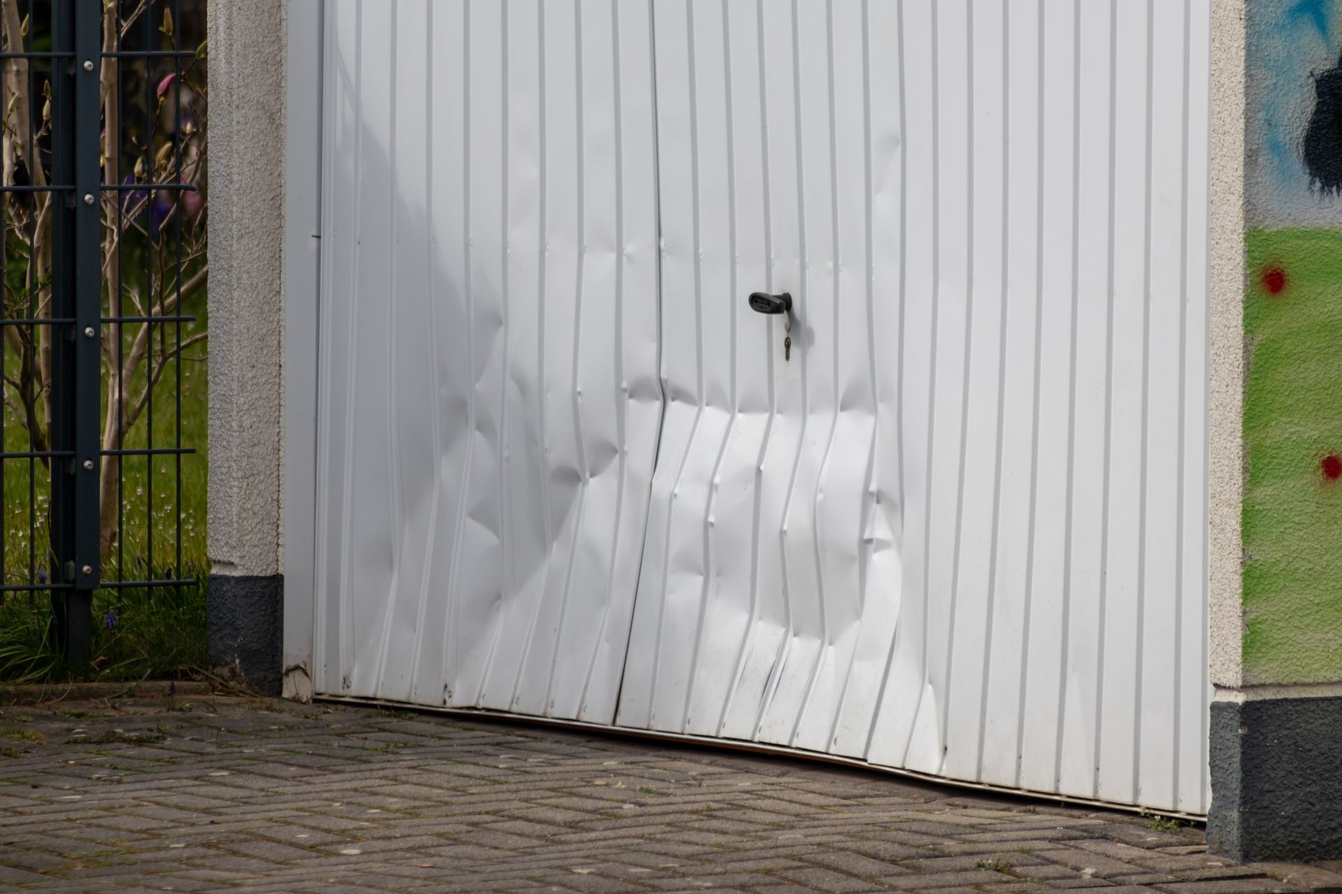 Damaged white garage door with significant dents and a lock.
