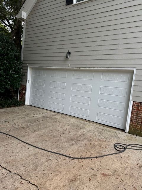 White garage door on a gray house with cracked concrete driveway. Black cable on the ground.