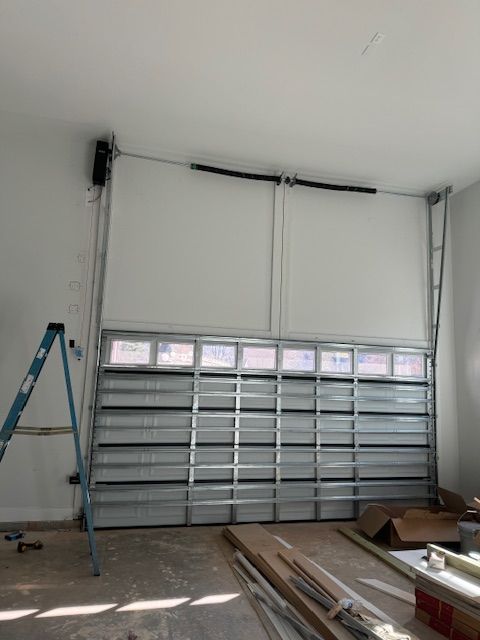 A garage door partially open inside a room, with a ladder to the left.