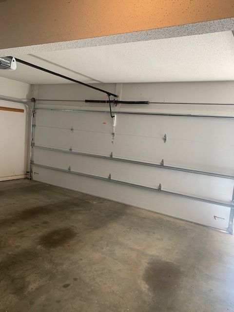 White garage door in partially open position, inside a garage with concrete floor.