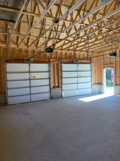 Garage interior with two white garage doors, concrete floor, and wooden beams.