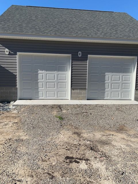 Two white garage doors on a gray-sided building with gravel driveway.