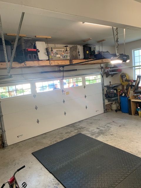 Garage interior with overhead storage, white garage door, and black floor mat.