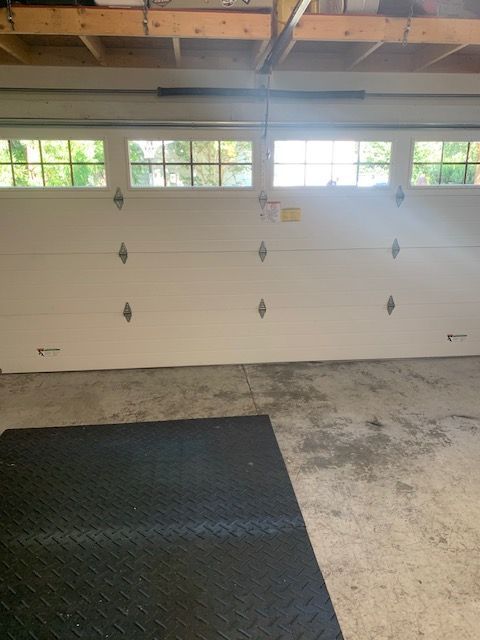A garage door closed inside a garage with windows and a black mat.