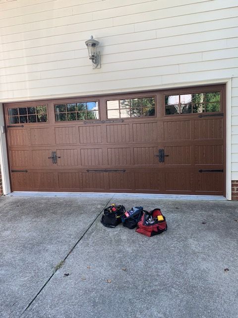Brown garage door with tool bags on concrete driveway.