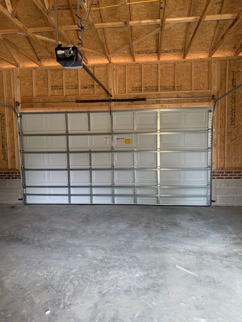 Garage interior with open white garage door. Exposed wood framing and concrete floor.