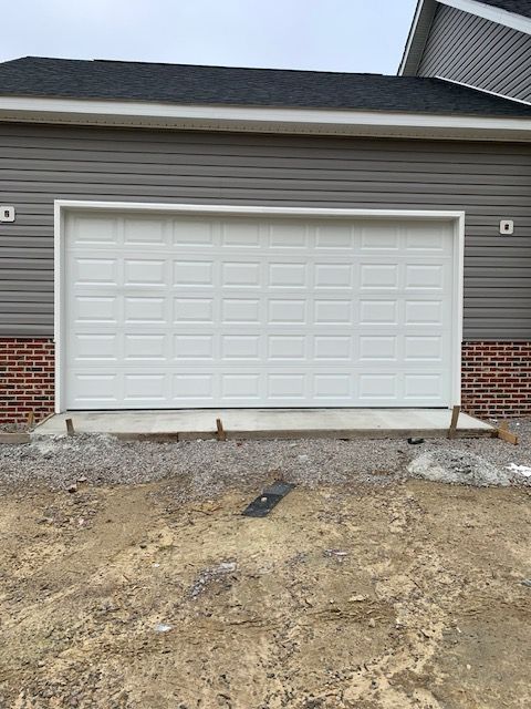 White garage door on a gray and brick building. Dirt and gravel in foreground.