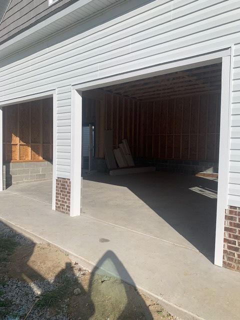 Unfinished garage exterior with two bays. Concrete floor, wooden frame interior, and light siding.