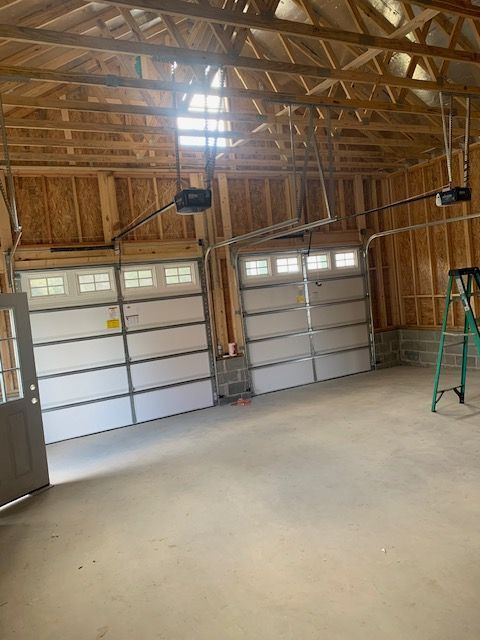 Two garage doors in a wood-framed garage. Garage door openers installed. Green ladder on the right.
