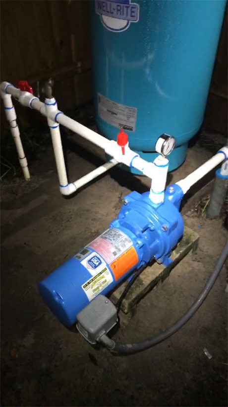 A blue well pump connected to a large light-blue pressure tank via white PVC piping, with a pressure gauge attached.