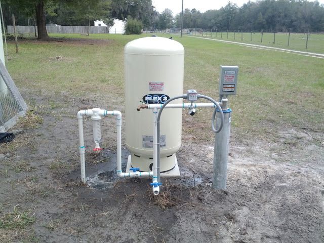 A well-tank and water filtration system setup with PVC piping installed outdoors on a grassy field.